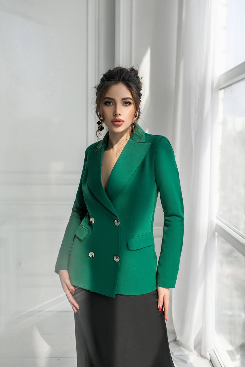 Woman wearing a green blazer in a bright room with white curtains.