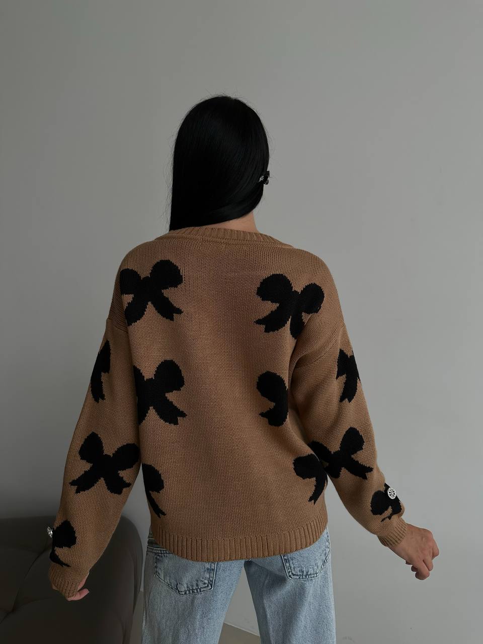 Person wearing a brown sweater with black bow patterns against a plain background