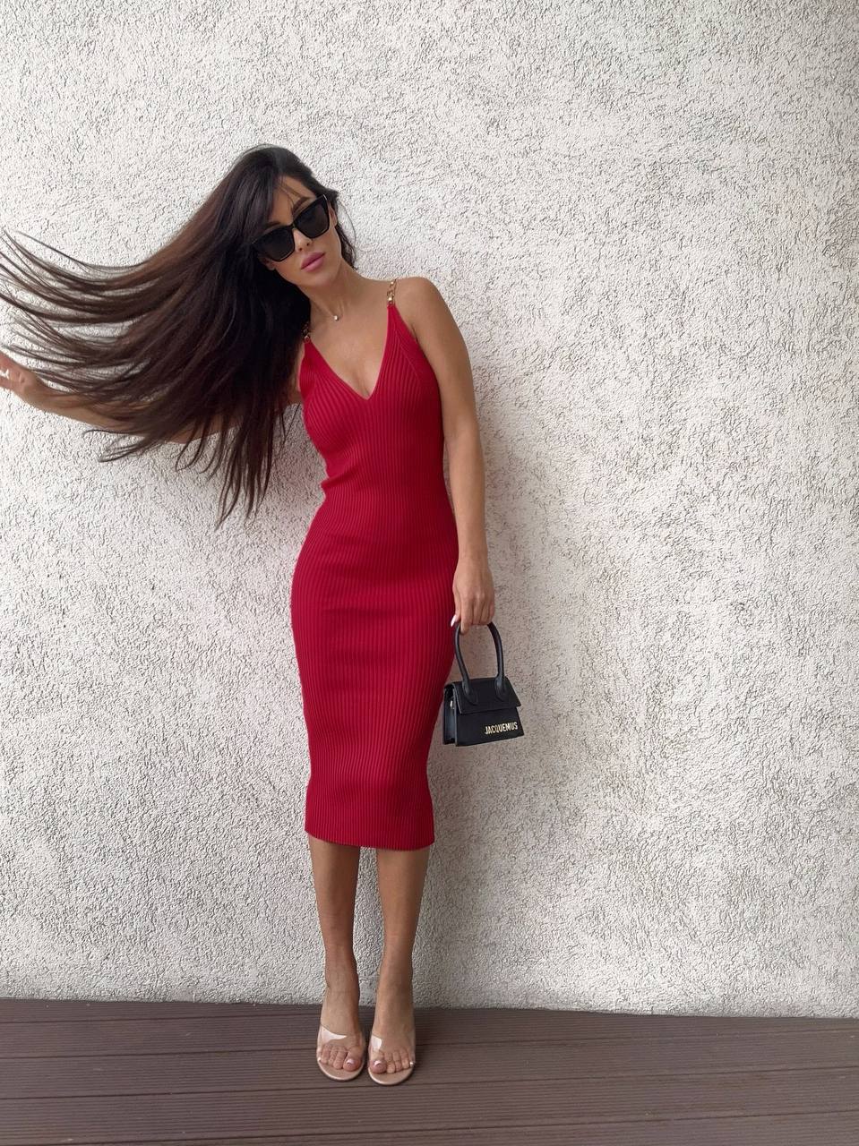 Woman in a red dress and sunglasses against a textured white wall.