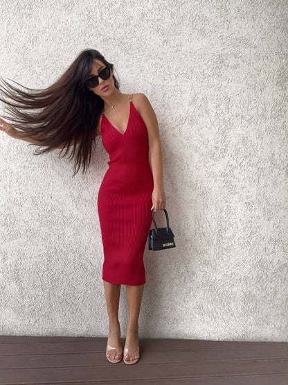 Woman in a red dress and sunglasses against a textured white wall.
