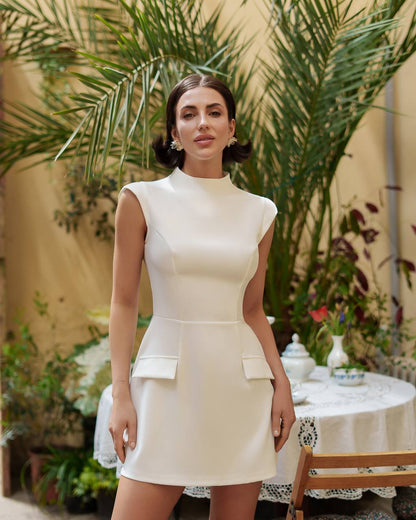 Woman in a white dress standing in an outdoor setting with plants and a table.