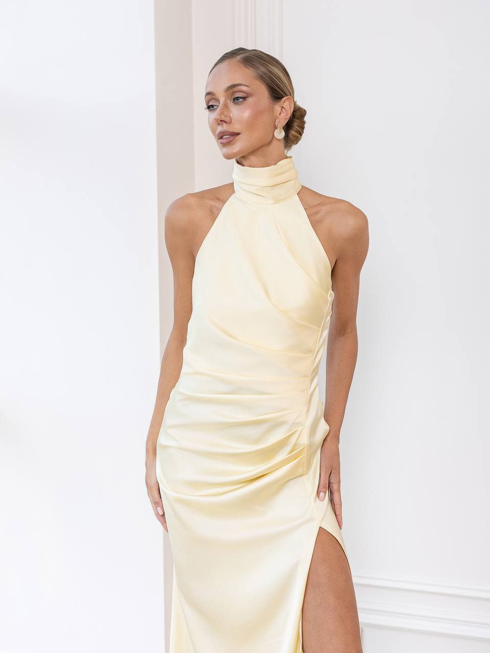 Woman wearing a light yellow halter neck dress with a slit on a white background