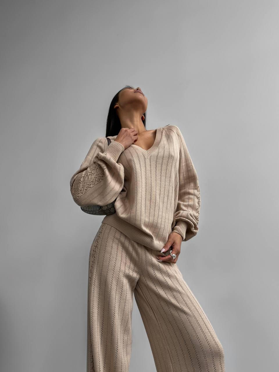 Person wearing a beige ribbed sweater and pants against a gray background