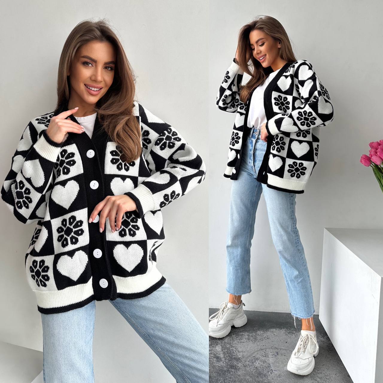 Woman wearing a black and white patterned cardigan with hearts and flowers, standing against a plain background.