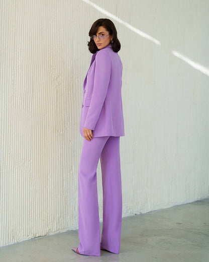 Woman wearing a lavender suit standing against a white wall.