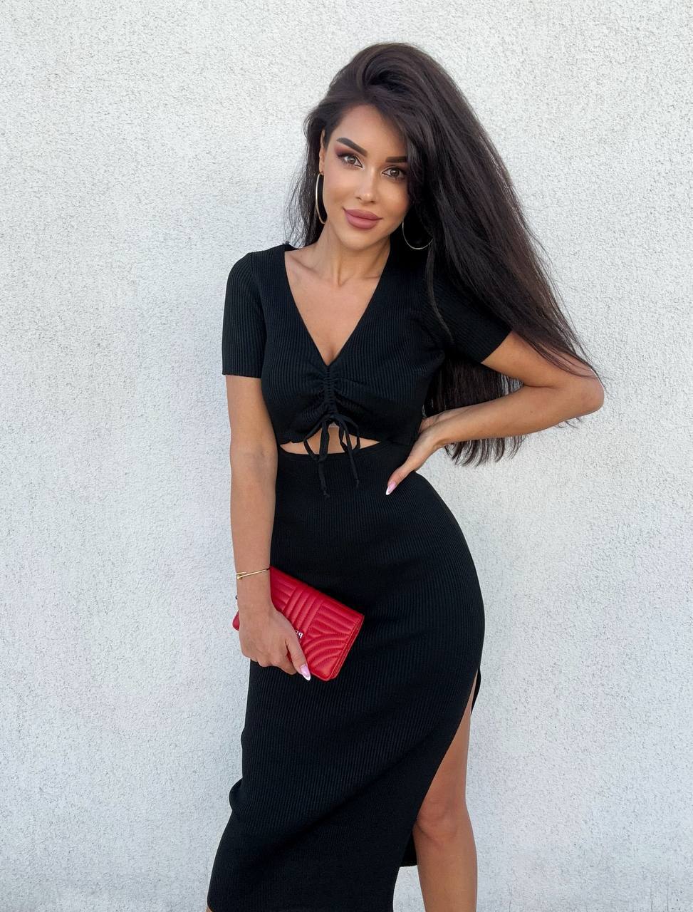 Woman in a black dress holding a red clutch against a light gray background