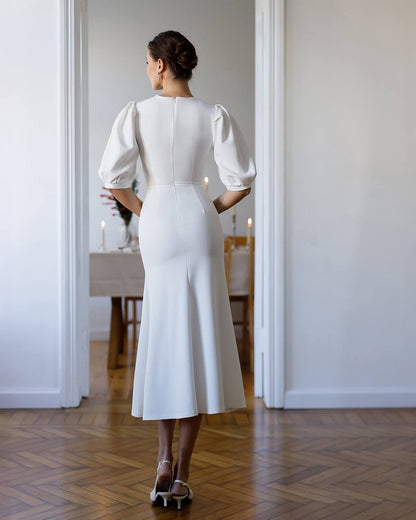 Woman in a white dress standing in a room with a dining table in the background