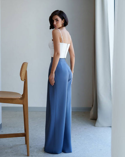 Woman wearing a white top and blue pants in a minimalistic room.