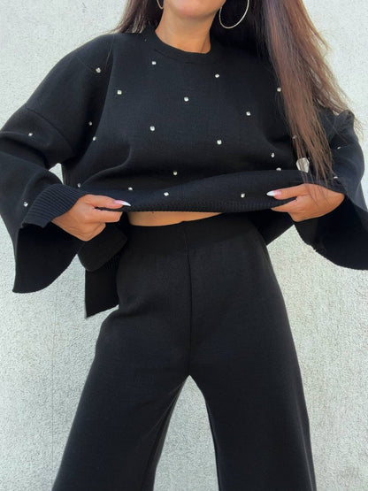 Person wearing a black sweater with white polka dots and black pants against a light gray background