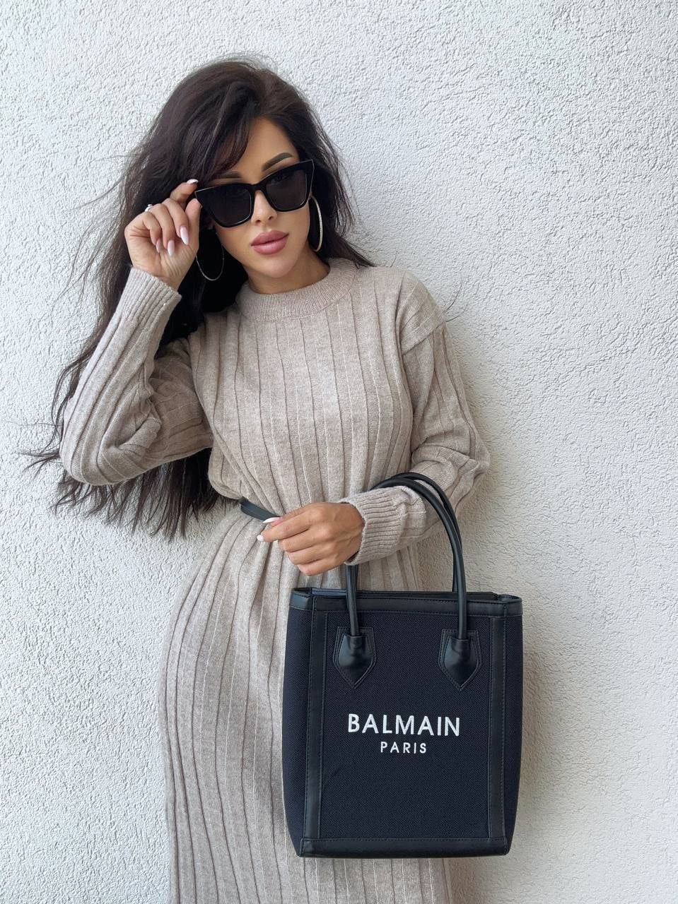 Woman holding a Balmain handbag against a white wall