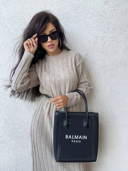 Woman holding a Balmain handbag against a white wall