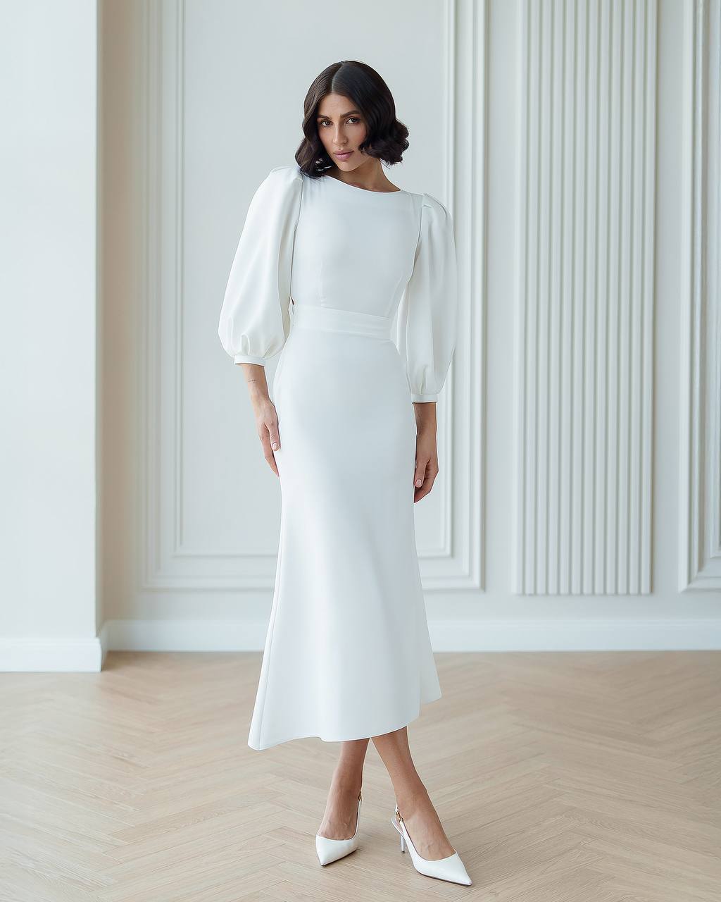 Woman wearing a white dress with puffed sleeves in a minimalistic setting