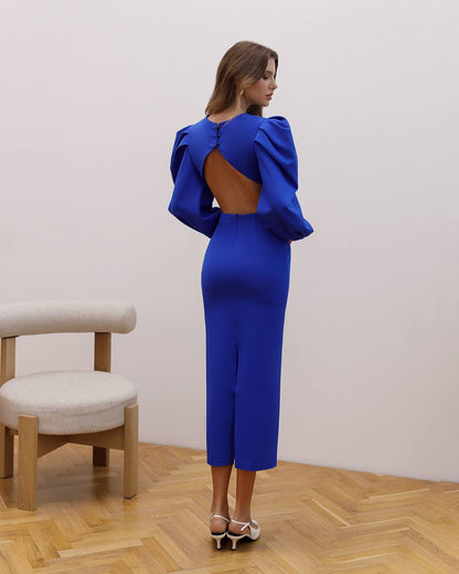 Woman wearing a blue dress with ruffled shoulders in an indoor setting.