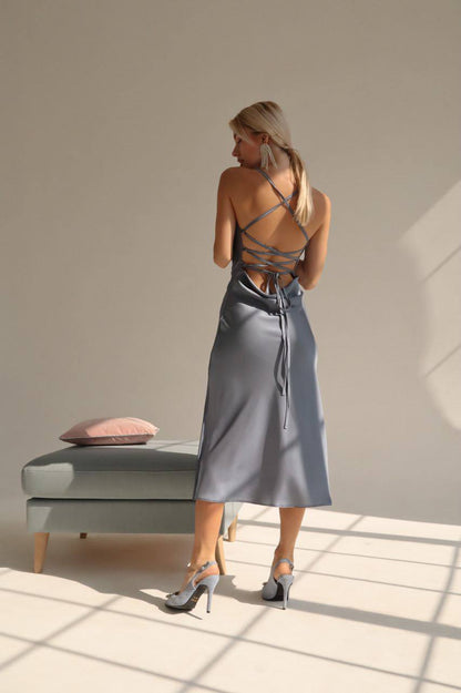 Woman in a gray slip dress standing in a sunlit room with a neutral color palette.