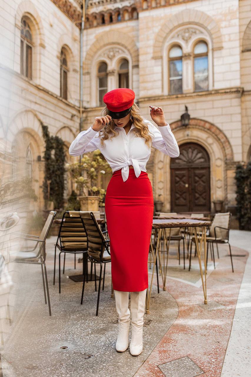 Woman in a red dress and white blouse standing in front of an old building with tables and chairs.