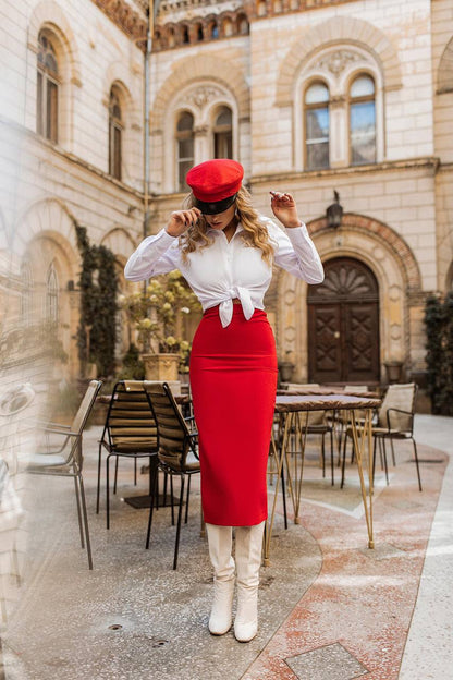Woman in a red dress and white blouse standing in front of an old building with tables and chairs.