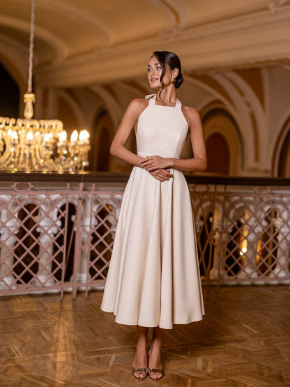 Woman in a white dress standing in an elegant indoor setting with chandeliers.