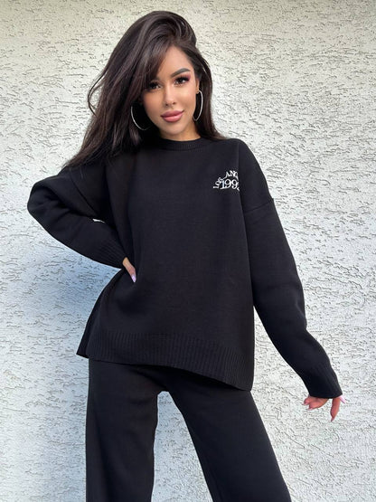 Woman wearing a black sweater with a logo against a textured wall.