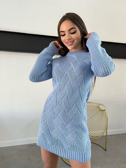 Woman wearing a blue knitted dress against a white wall.