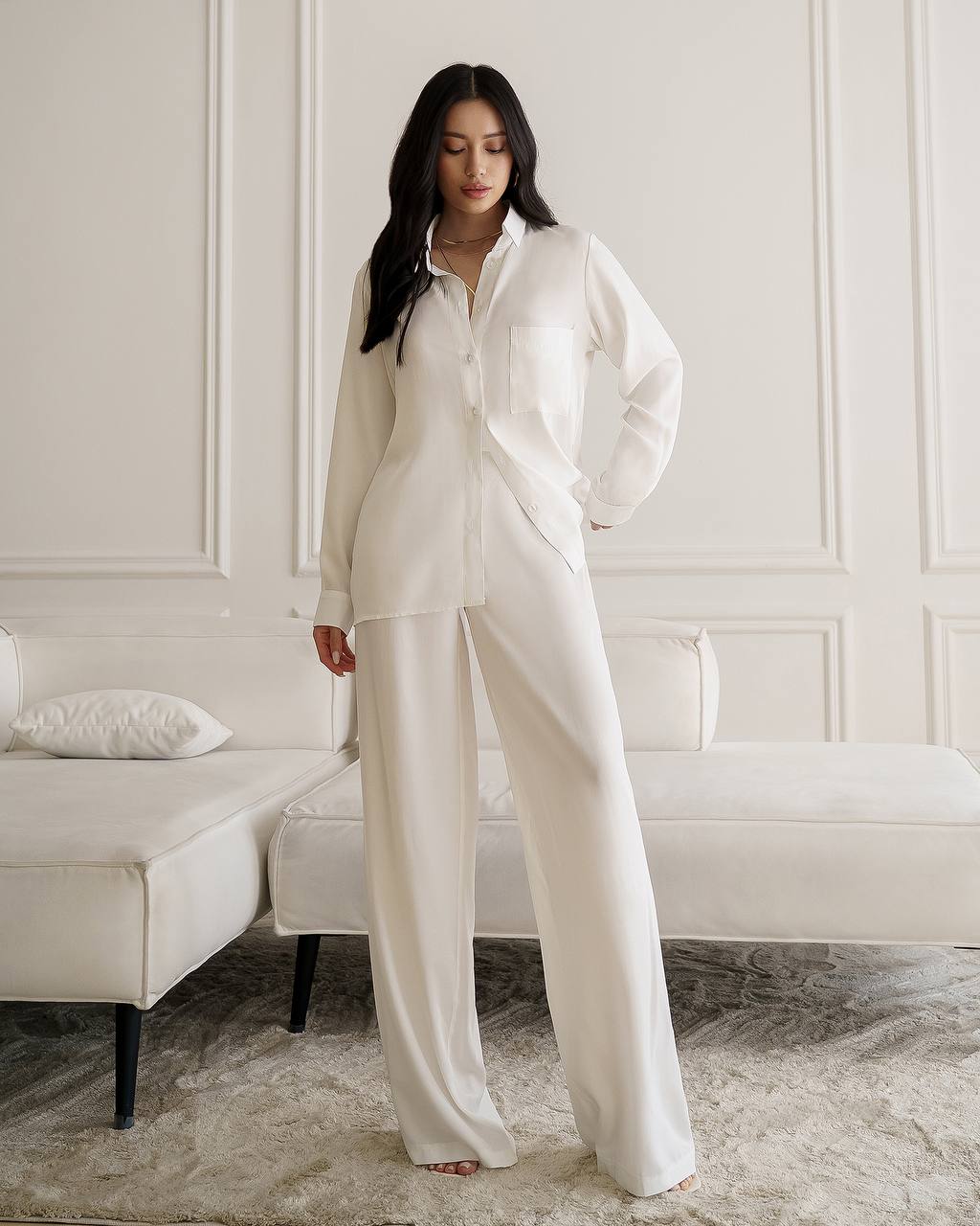Woman wearing a white pajama set in a room with a white sofa.