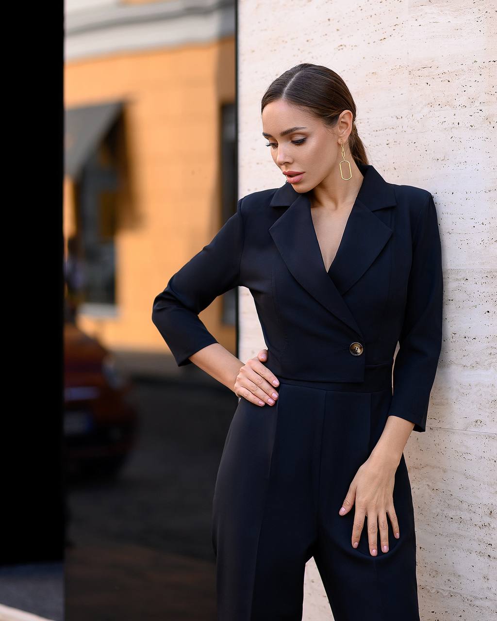 Woman in a black suit standing against a textured wall.