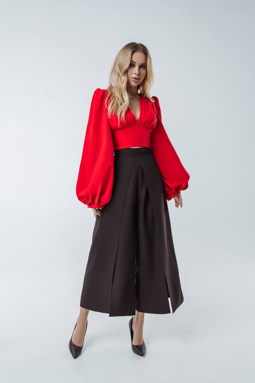 Woman wearing a red blouse with balloon sleeves and black high-waisted pants on a white background