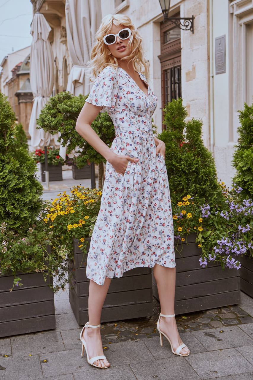Woman in a floral dress standing outdoors with plants and flowers in the background