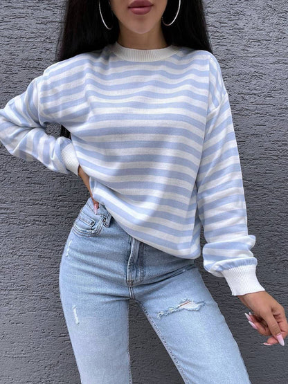 Person wearing a blue and white striped sweater and light blue jeans against a gray wall.
