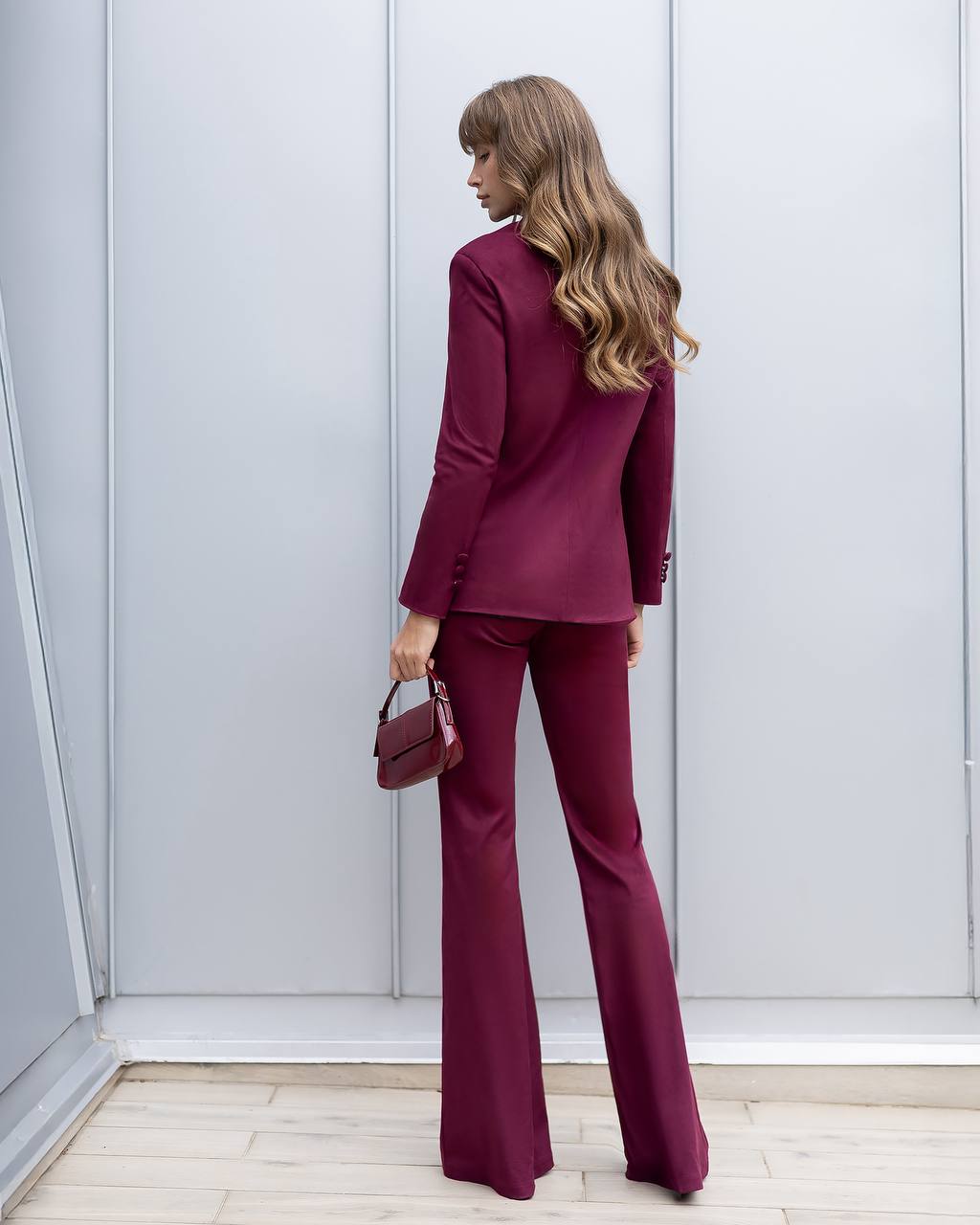 Woman in a burgundy suit standing against a light gray wall.