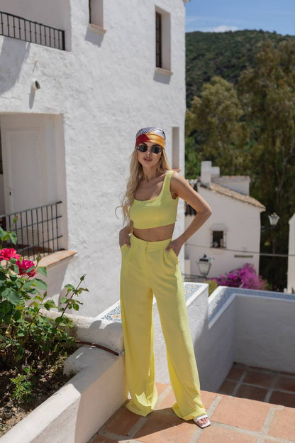 Woman in yellow outfit standing on a terrace with white building and greenery in the background