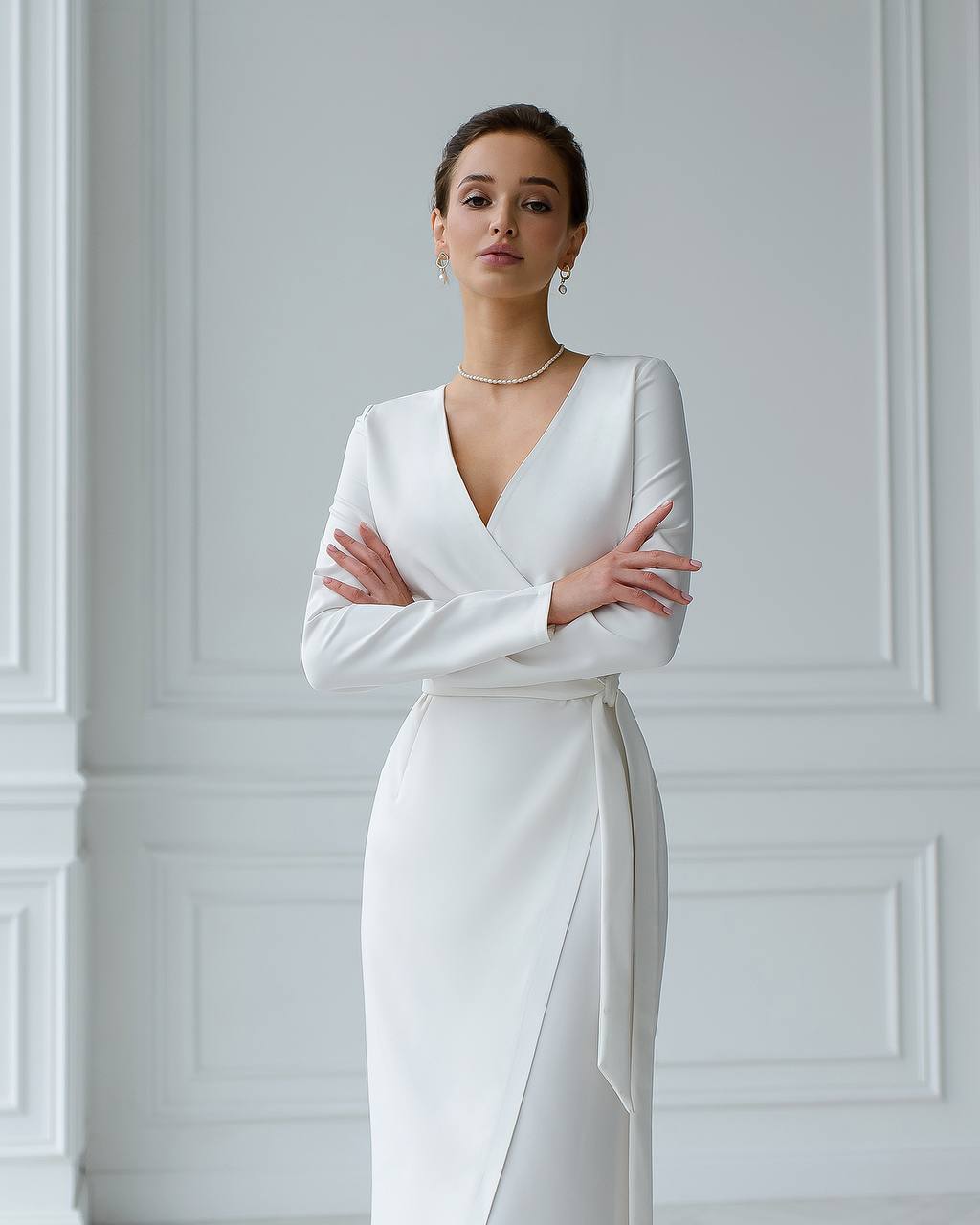 Woman wearing a white dress with long sleeves against a white wall