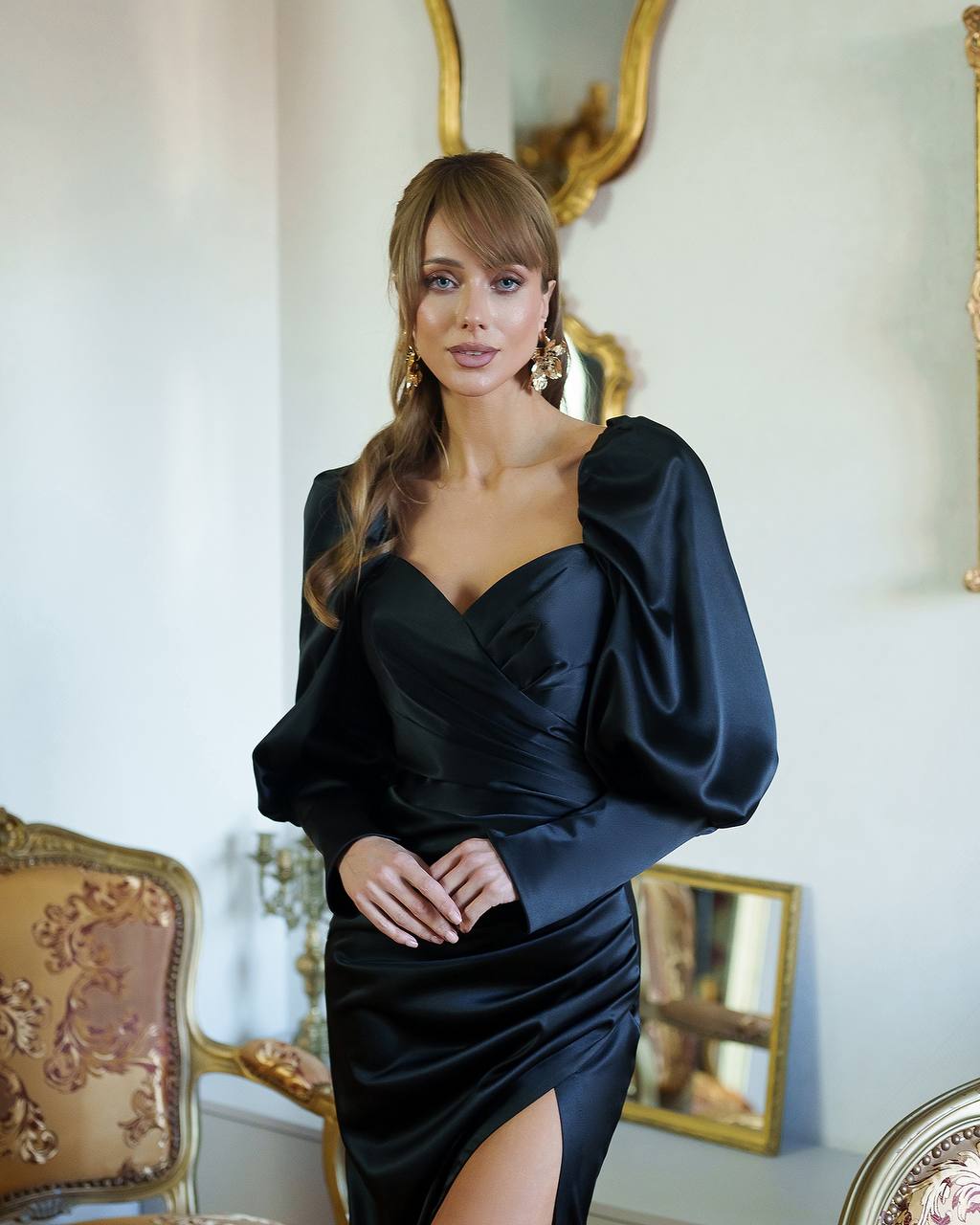 Woman in a black dress standing in an elegant room with gold accents.