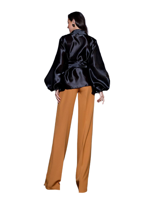 Person wearing a black satin jacket and mustard yellow pants on a white background