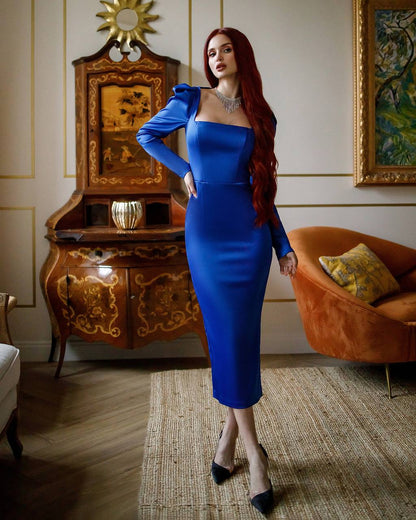 Woman in a blue dress standing in an elegant room with ornate furniture and a painting.