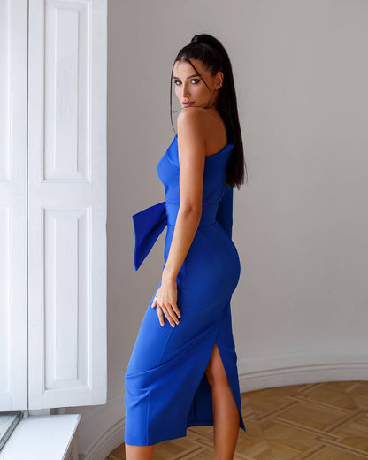 Woman wearing a blue dress with a bow detail in an indoor setting.