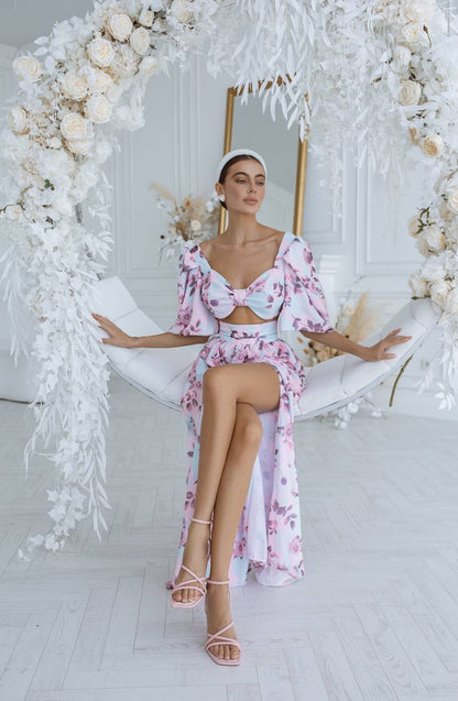 Woman in a floral dress sitting on a swing surrounded by white flowers and decor.