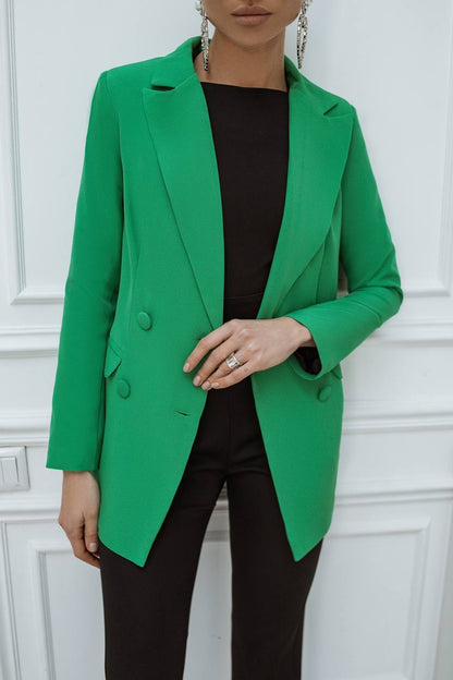 Person wearing a green blazer over a black top against a white paneled wall.