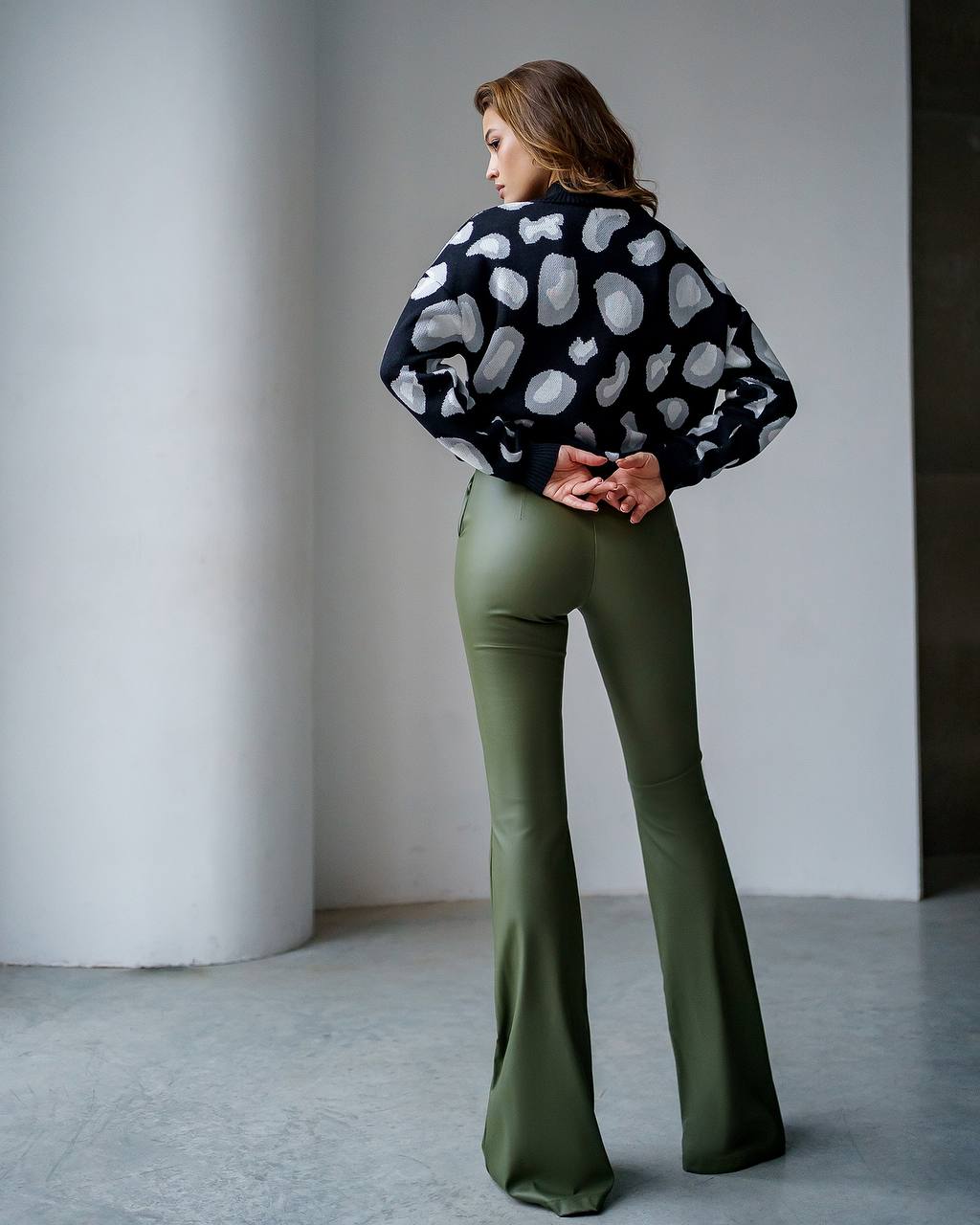Woman wearing a black and white patterned sweater and green flared pants against a plain background