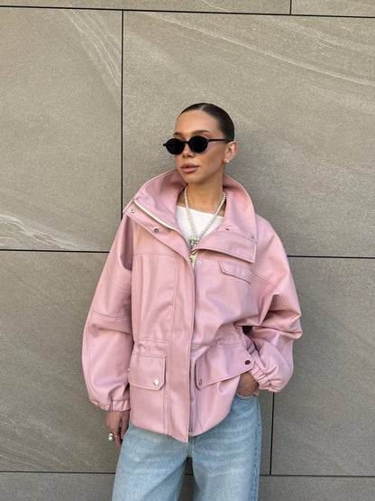 Person wearing a pink jacket and sunglasses against a gray wall