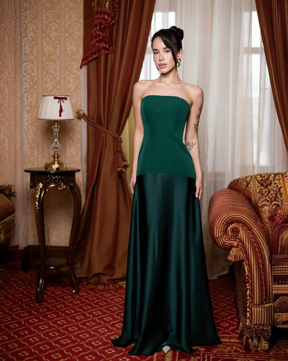 Woman in a green strapless gown standing in an elegant room with red curtains and patterned carpet.