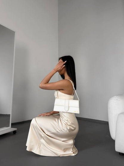 Woman in a white dress sitting on the floor with a white handbag, in a minimalistic room.