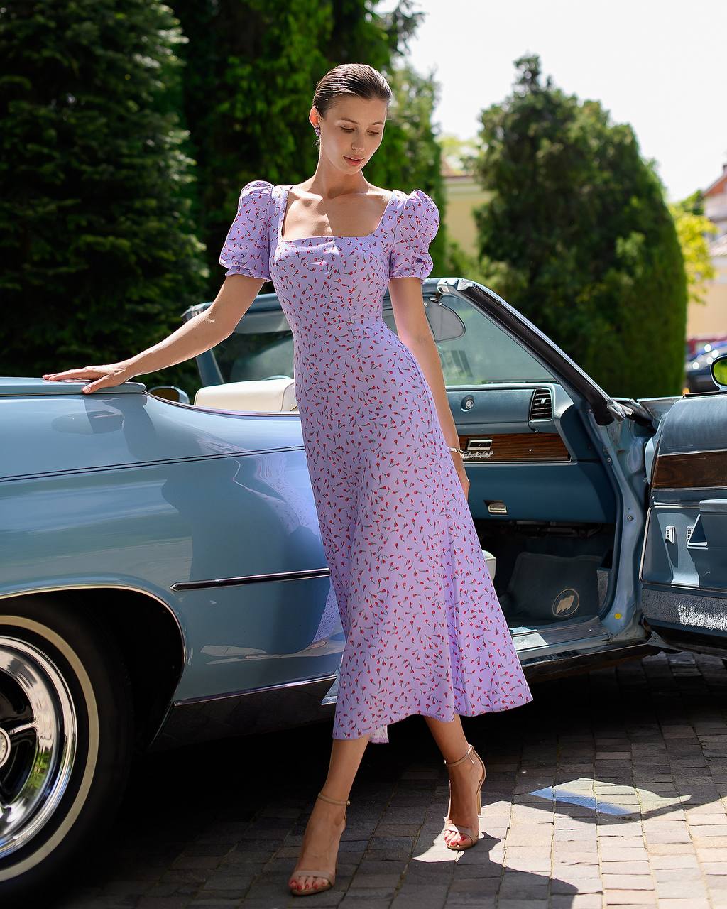 Woman in a purple floral dress standing next to a vintage car