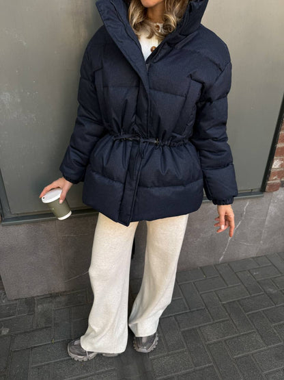 Person wearing a navy blue puffer coat holding a coffee cup on a sidewalk.