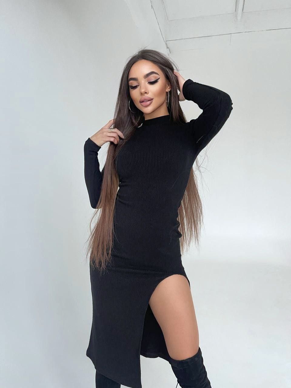 Woman wearing a black dress with a slit, standing against a white background