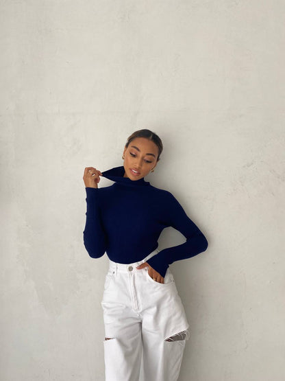 Person wearing a navy turtleneck and white pants against a plain background