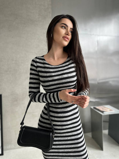Woman wearing a black and white striped dress holding a black handbag indoors.