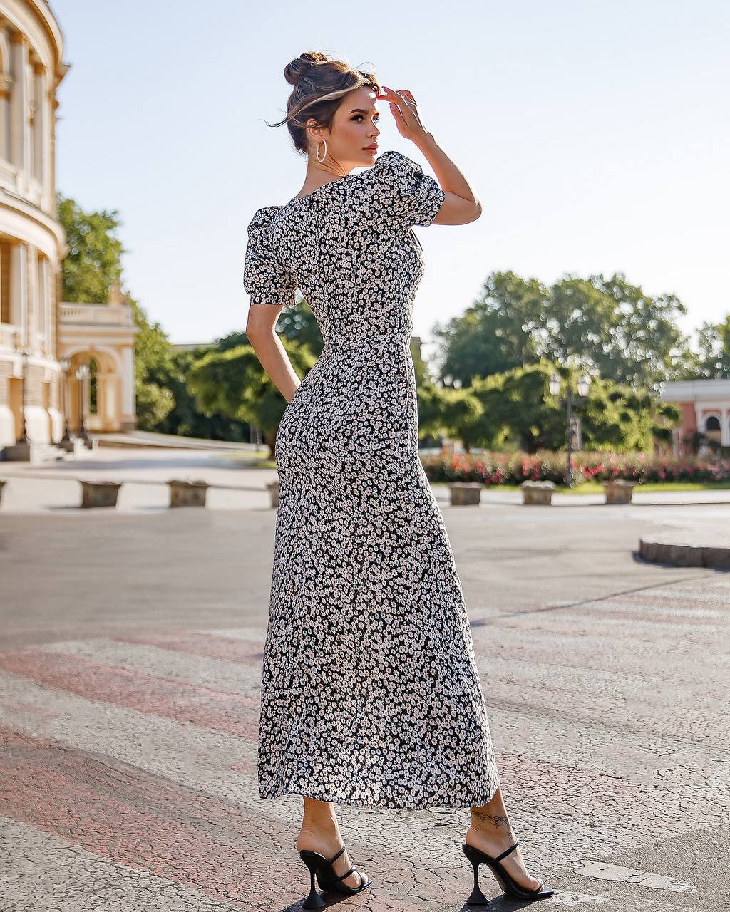Woman in a floral dress standing outdoors with trees and buildings in the background