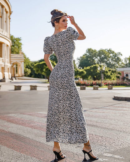 Woman in a floral dress standing outdoors with trees and buildings in the background