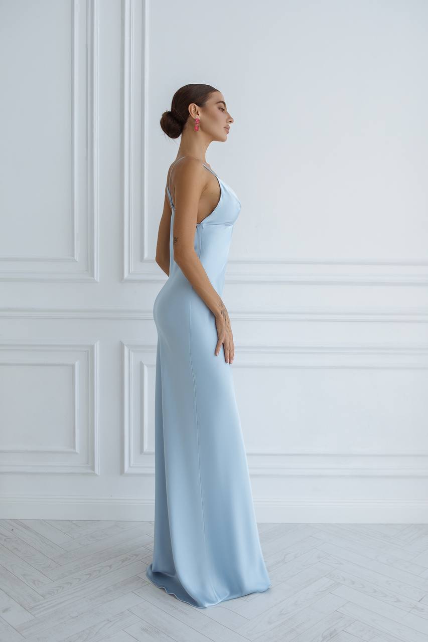 Woman in a light blue evening gown standing against a white wall.