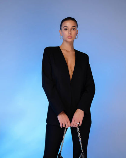 Person wearing a black suit with a deep neckline against a blue gradient background